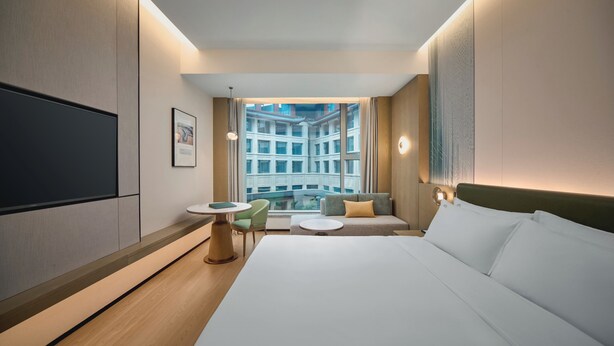 A modern hotel room with a large bed, a small table, a sofa, and a TV on the wall. - Holiday Inn Wuhan Tianhe Airport by IHG (Wuhan)