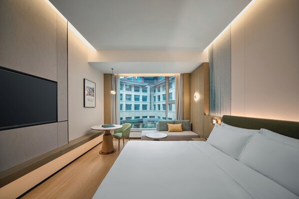 Una habitación de hotel moderna con una cama grande, una mesita, un sofá y un televisor en la pared.