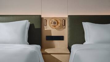 A hotel room with two beds, a wooden headboard, a small wooden table, and a wall-mounted control panel.