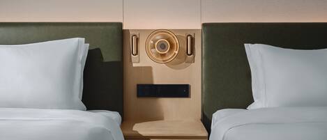 Habitación de hotel con dos camas, cabecero de madera, una mesita pequeña y un panel de control en la pared.
