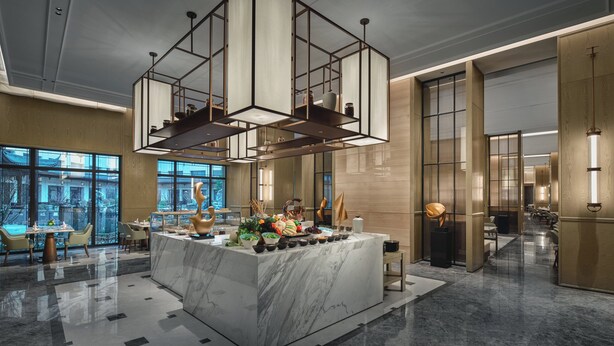 A modern hotel lobby with a marble reception desk, a geometric hanging light fixture, and large windows offering a view of the city. - Holiday Inn Wuhan Tianhe Airport by IHG (Wuhan)