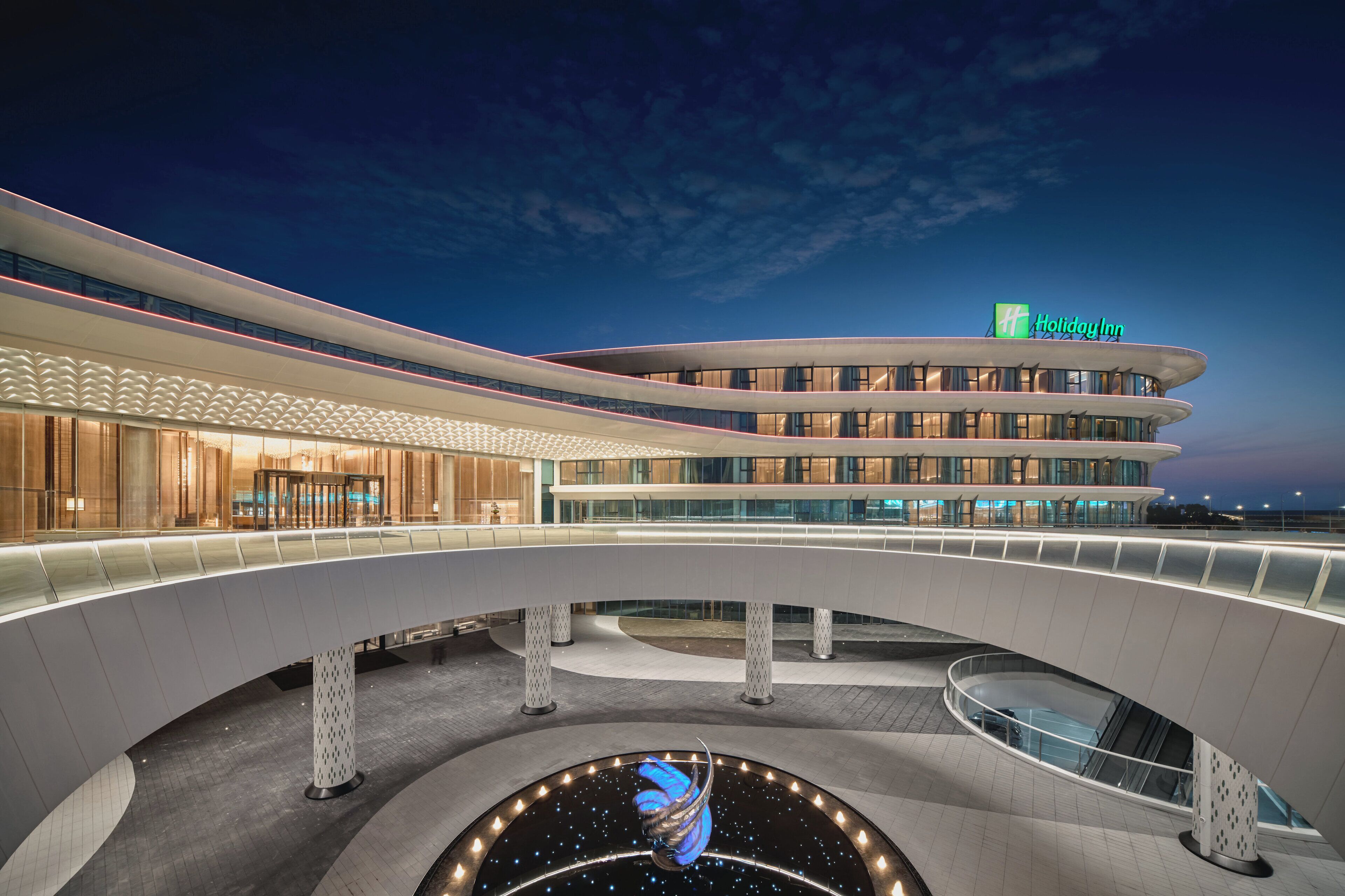 A modern hotel with a curved facade, a prominent Holiday Inn sign, and a central atrium with a unique spiral sculpture.