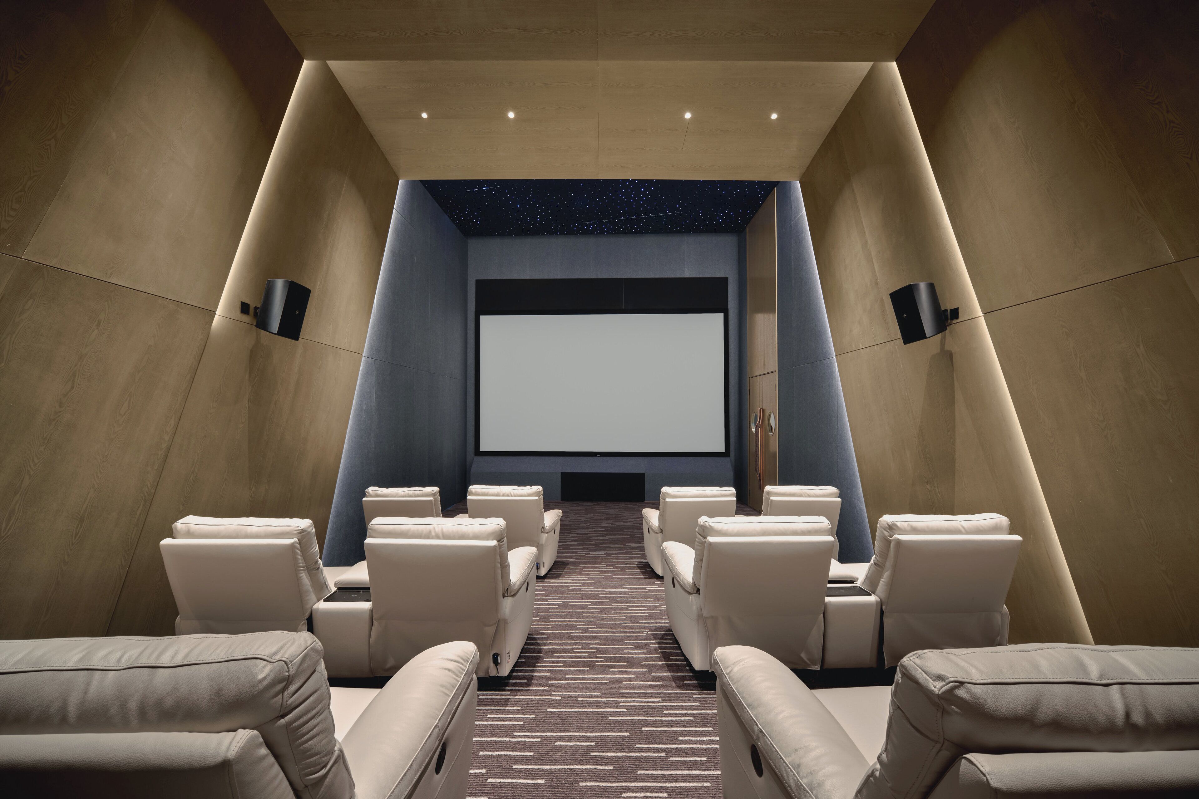 A modern home theater with plush seating, a large screen, and a starry ceiling.