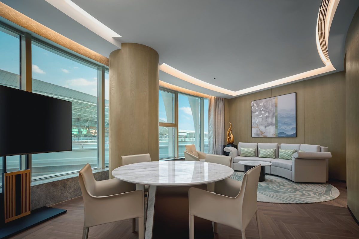 A modern hotel room with a large window, a round dining table, and a sofa.