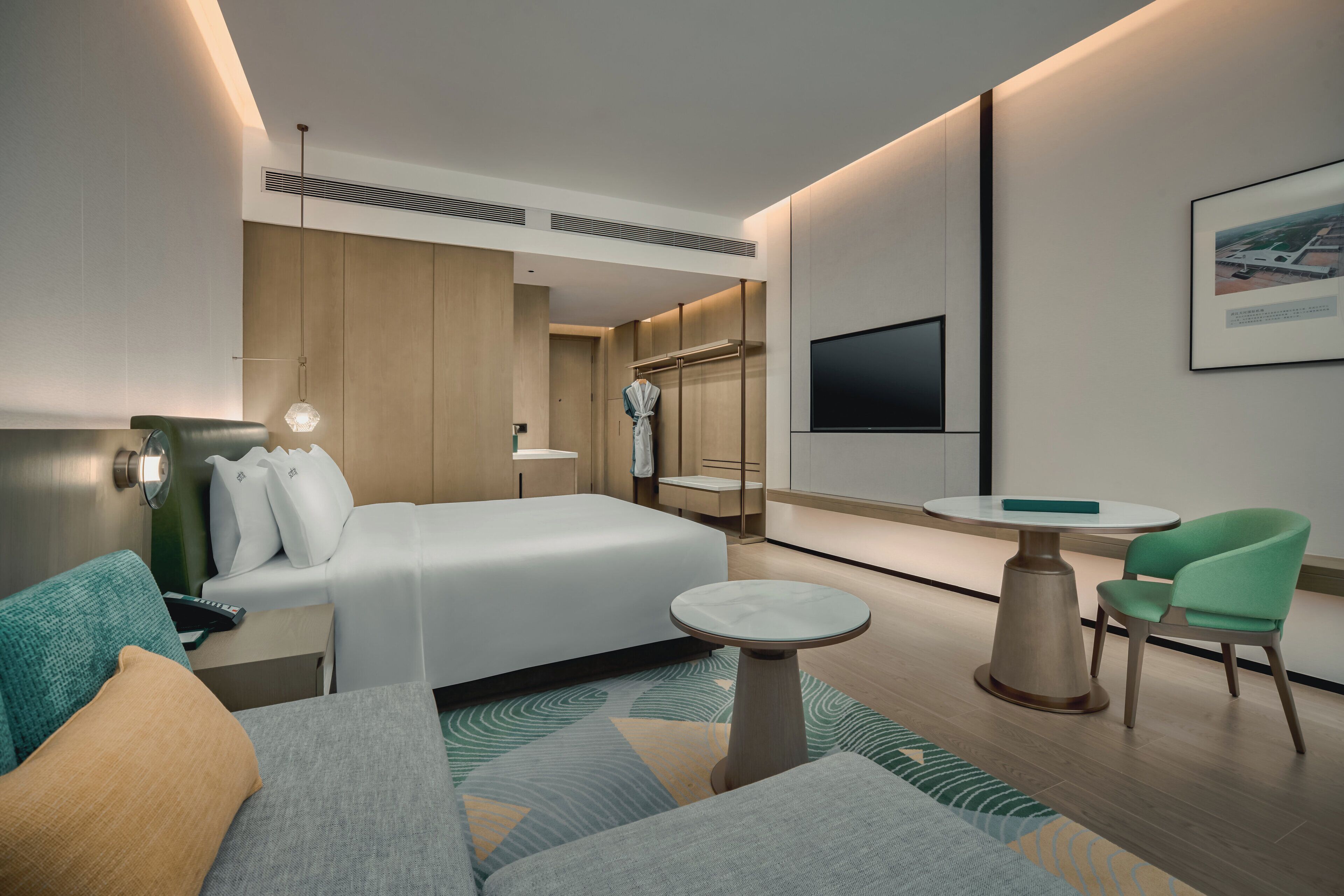 Een moderne hotelkamer met een bed, een zithoek met een tafel en stoelen, een aan de muur bevestigde televisie, en een badjas hangend op een rek.