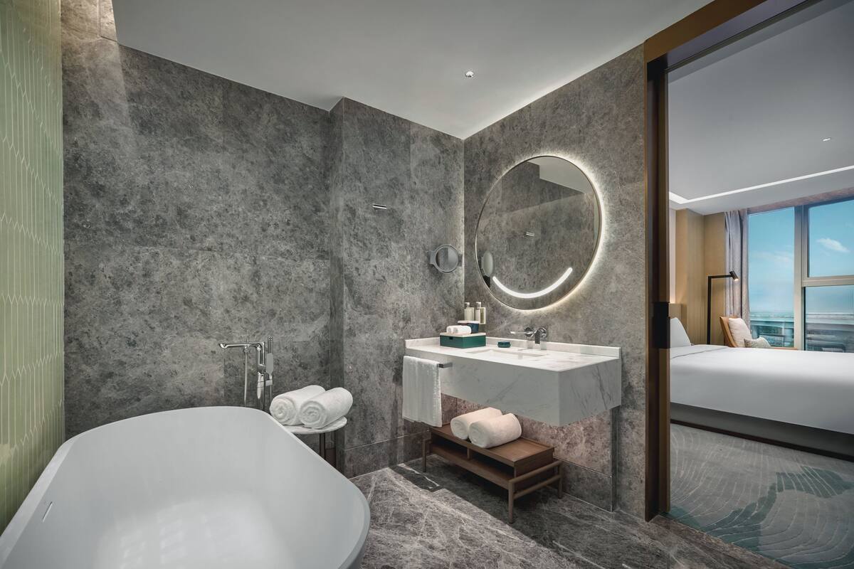 Un baño moderno con una bañera independiente, un tocador con espejo y un amplio ventanal con vistas a la ciudad.