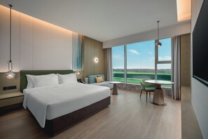 A modern hotel room with a large bed, a small table, a sofa, and a view of a green landscape through large windows. - Holiday Inn Wuhan Tianhe Airport by IHG (Wuhan)