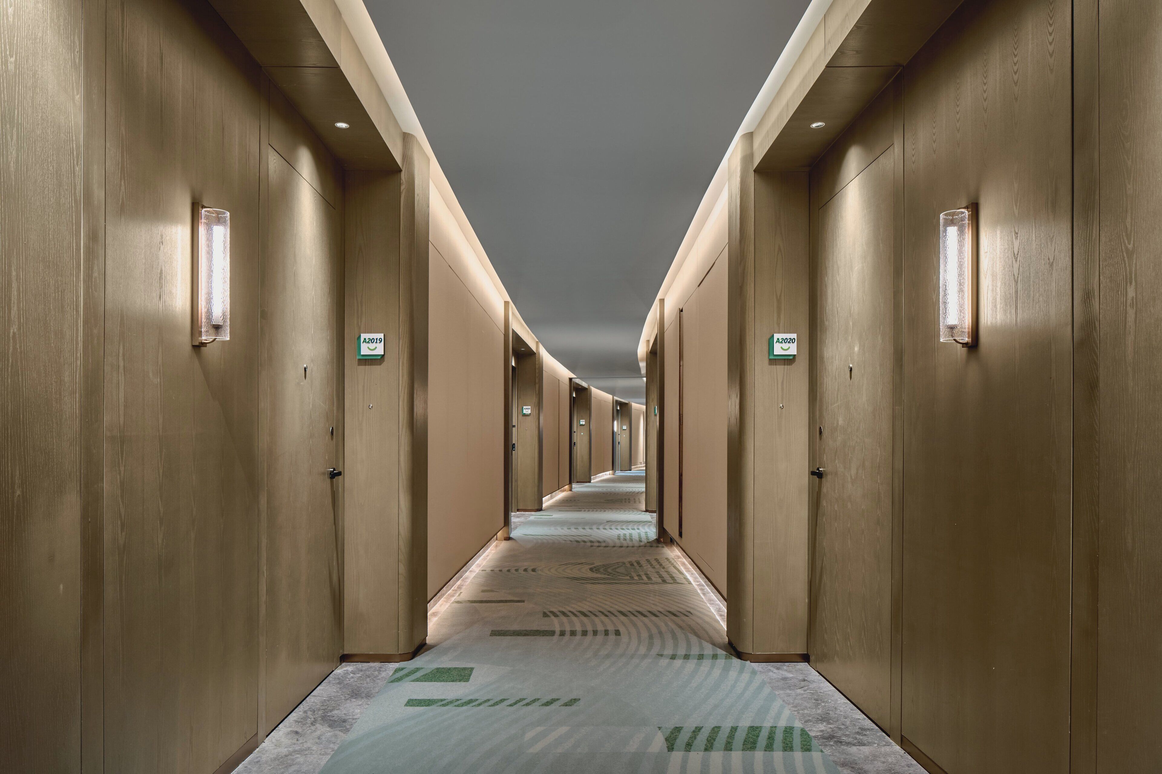 A long, narrow hotel corridor with wooden walls and doors, each marked with a number.