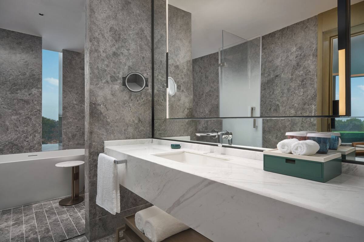 Un baño moderno con un espejo grande, una bañera y un tocador con lavabo y espacio para toallas.