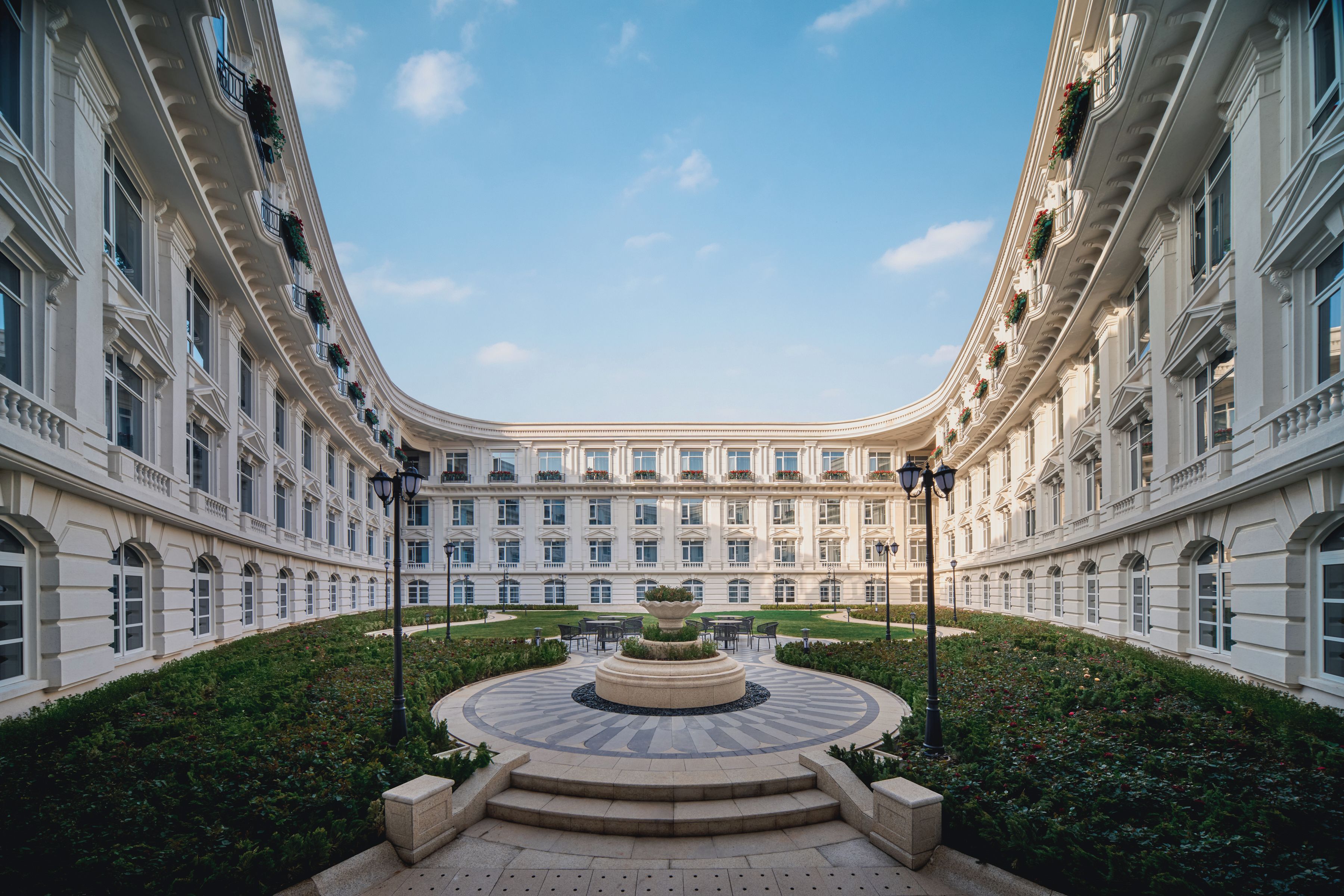 A grand hotel courtyard with a central fountain, symmetrical architecture, and lush greenery.