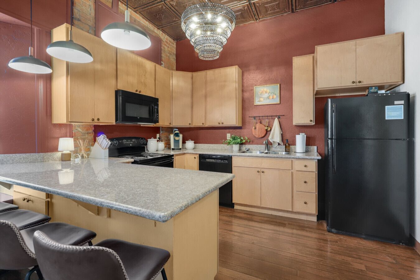 A kitchen with wooden cabinets, a black refrigerator, a granite countertop, and a chandelier.