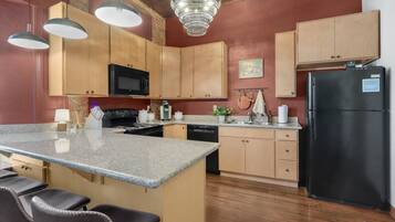 A kitchen with wooden cabinets, a black refrigerator, a granite countertop, and a chandelier.