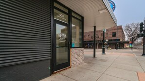 Une devanture de magasin avec un volet métallique fermé, un bâtiment en briques portant une enseigne indiquant « 428, avenue Central », et un logo circulaire bleu avec le mot « PIPER » sur un bâtiment en arrière-plan.
