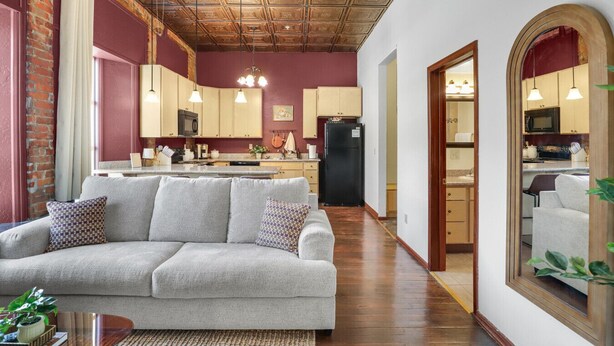 Un salon moderne avec un canapé gris, un plafond en bois et une cuisine en arrière-plan.