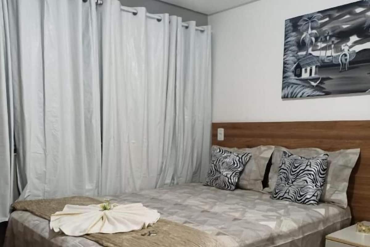 Een slaapkamer met een groot bed, twee kussens, een hoofdeinde, een nachtkastje en een schilderij aan de muur.