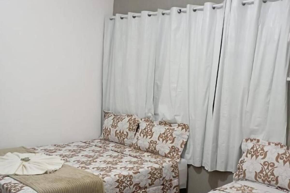 Een kamer met twee bedden, elk voorzien van beddengoed met een patroon en een witte gordijn.