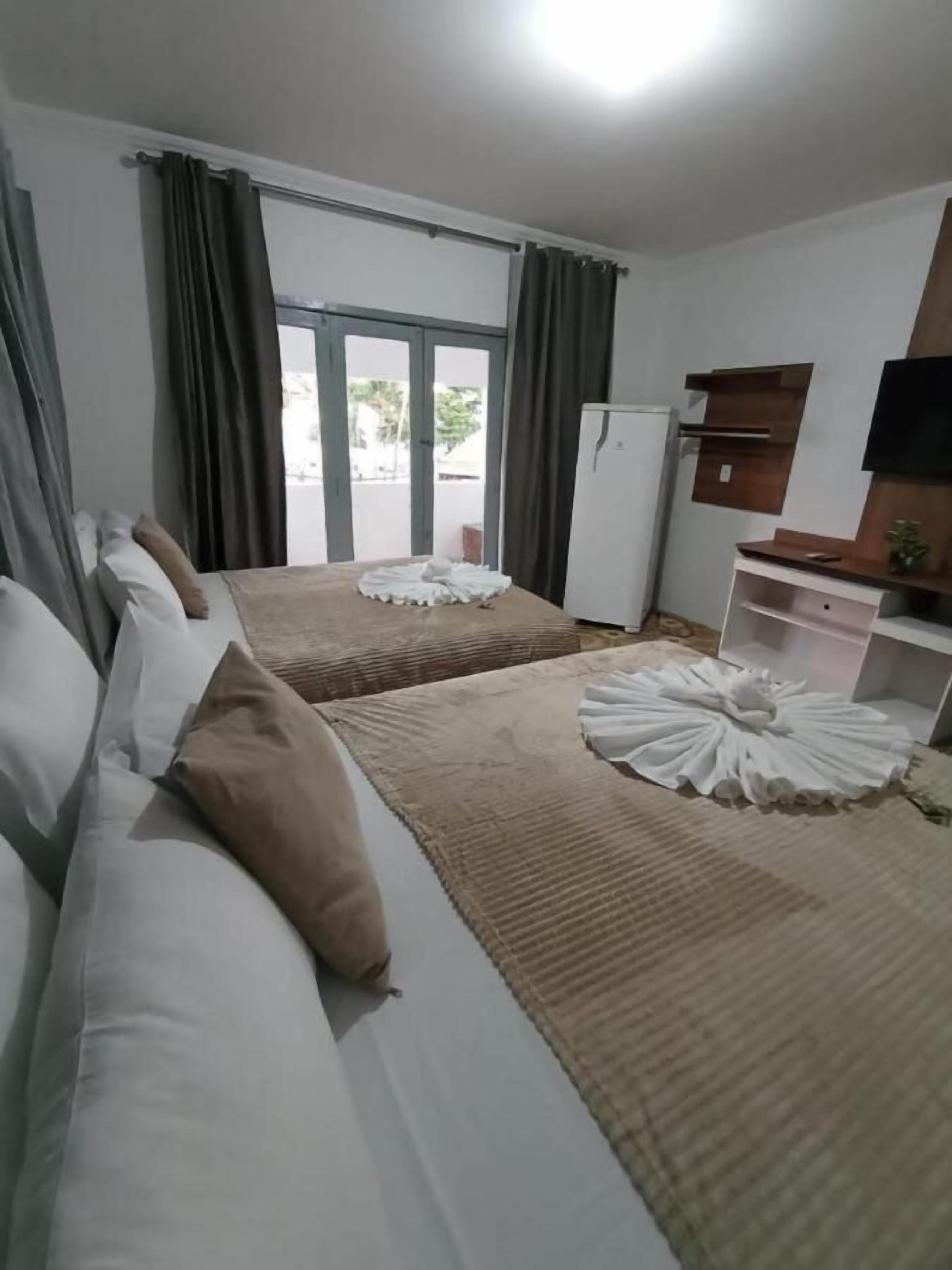 A hotel room with two beds, a flat-screen TV, a small kitchenette, and a view of the outdoors.