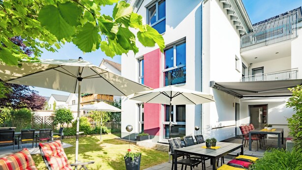 Eine moderne Außenpatio mit Esstisch, Stühlen und Sonnenschirmen.