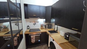 A compact kitchen with dark cabinets, a wooden countertop, a built-in oven, a sink, and a coffee machine.