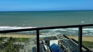 A view of the ocean from a window overlooking a beach with solar panels and industrial structures. - RN STUDIO - APTO 1008 (Maceio)