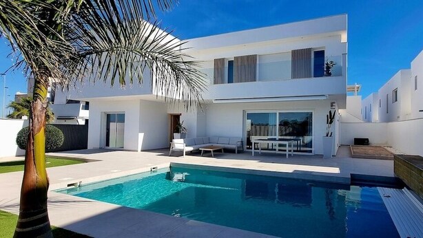 A modern two-story house with a swimming pool, a patio with seating, and a palm tree. - Villa Escara with private pool (San Javier)