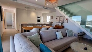 A modern living room with a sofa, a dining table, and a staircase leading to an upper level. - Villa Escara with private pool (San Javier)