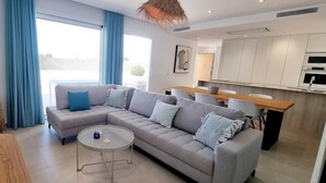 A modern living room with a grey sectional sofa, a round coffee table, and a dining area with a wooden table and chairs. - Villa Escara with private pool (San Javier)