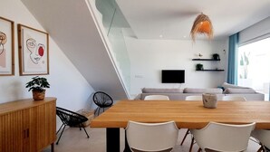 A modern dining area with a wooden table and white chairs, a sofa, and a TV on the wall. - Villa Escara with private pool (San Javier)