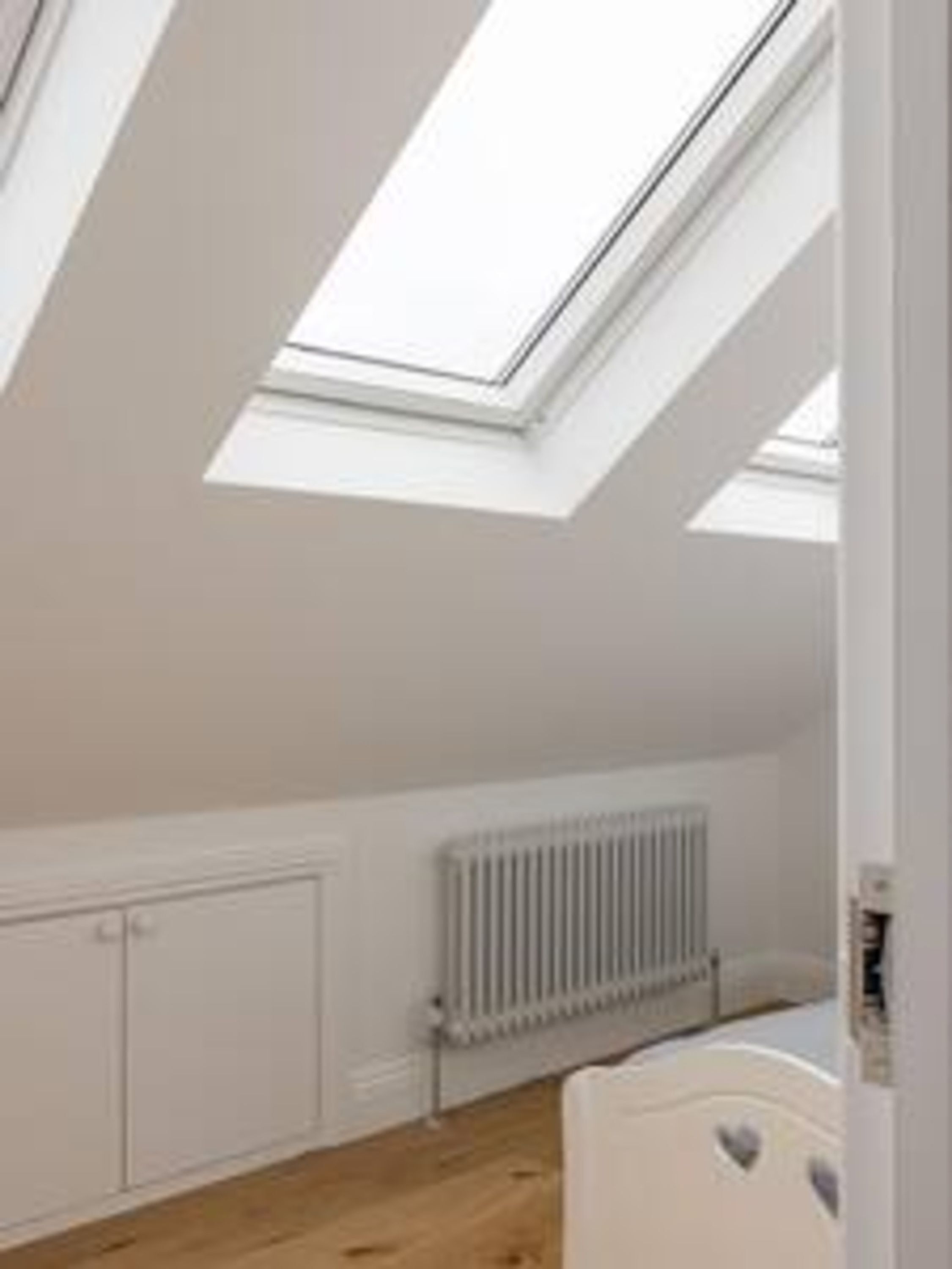 A room with a sloped ceiling, skylights, a radiator, and a white wardrobe.