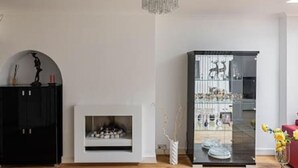 Ett modernt vardagsrum med en öppen spis, ett svart skåp, ett glasskåp och en röd soffa.