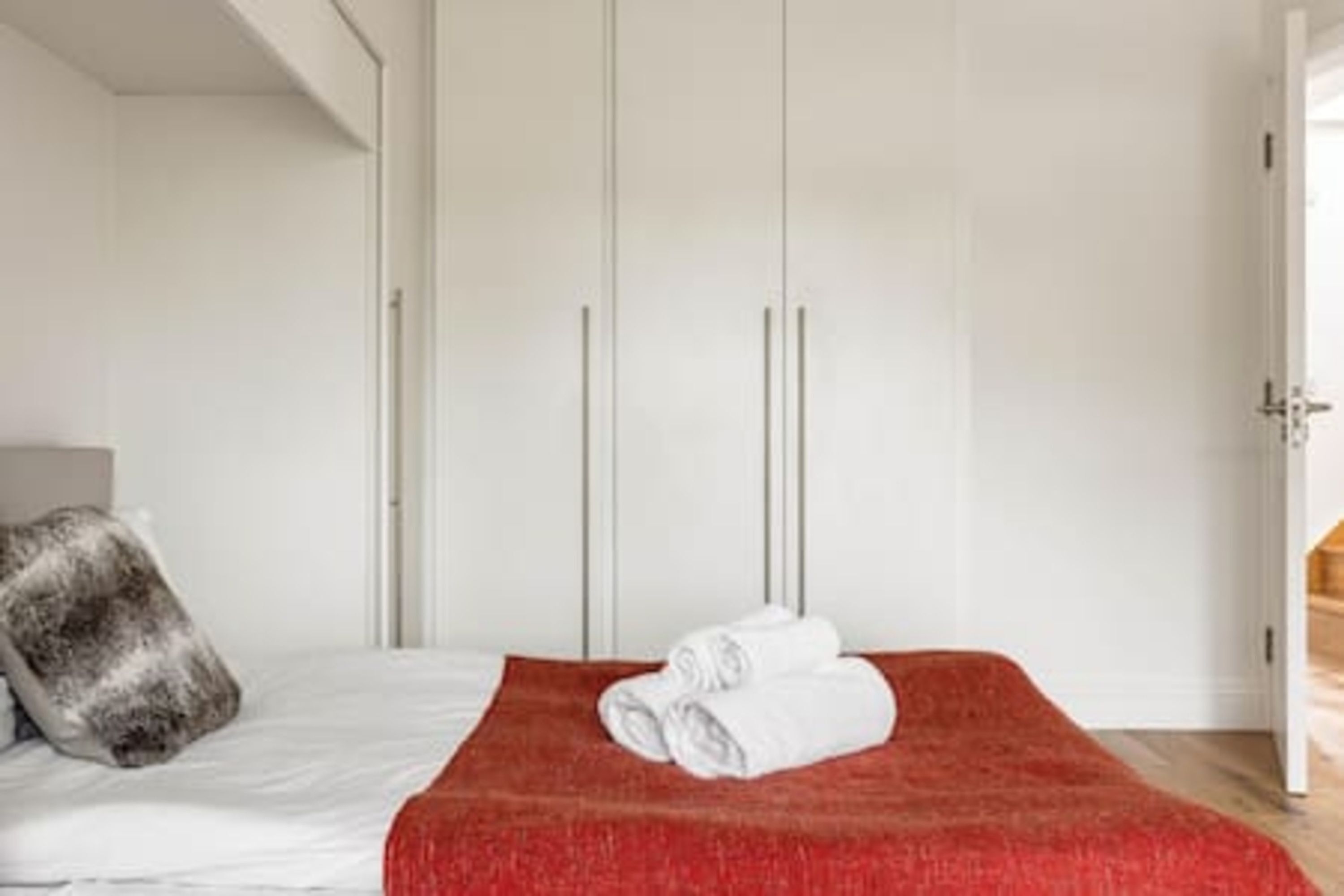 A hotel room with a bed, a red blanket, a white pillow, and a wardrobe.