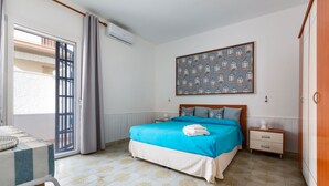 Ein Schlafzimmer mit einem Bett, einem Nachttisch, einem Sessel, einem Tisch und einem Fenster mit Vorhängen.