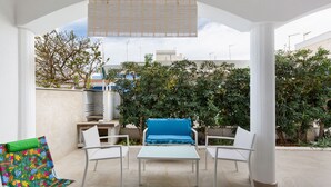 Eine Terrass mit blauer Couch, weißen Stühlen und einem bunten Sessel.