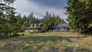 A two-story house with a porch and a deck, surrounded by dense forest. - A Re-styled Single Story, 3-bedroom, 2-bath Ranch Style Cabin at Silver Lake (Maple Falls)