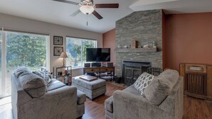 A modern living room with a flat-screen TV, two grey sofas, a ceiling fan, and a stone fireplace. - A Re-styled Single Story, 3-bedroom, 2-bath Ranch Style Cabin at Silver Lake (Maple Falls)