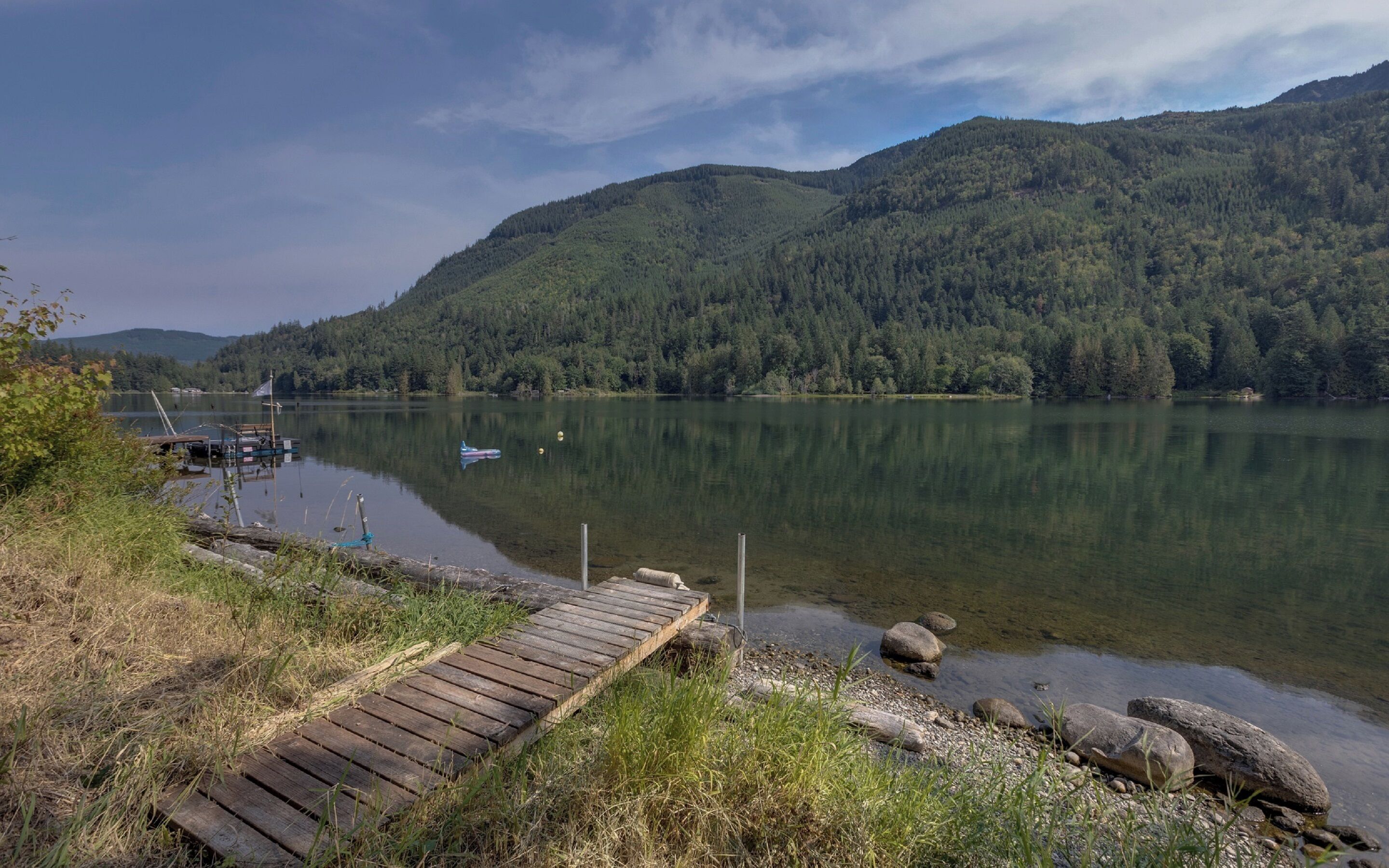 A wooden dock leading to a calm lake surrounded by forested hills.