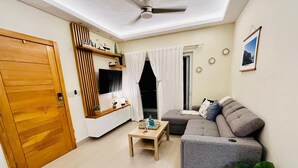 Un espace de vie compact avec une porte en bois, une petite table, un canapé gris et un ventilateur de plafond.