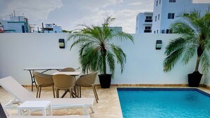 Un espace piscine aménagé sur le toit, avec des chaises longues, une table et des plantes en pot.