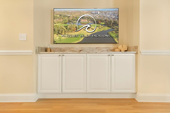 A kitchen with white cabinets, a marble countertop, and a framed picture of Wavecrest Beach Vacations.