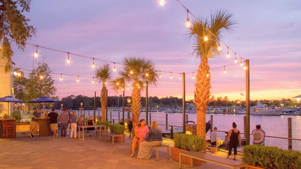 An outdoor seating area with string lights, palm trees, and a view of the marina.