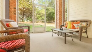 A sunlit patio with wicker furniture and a glass door leading to a garden.