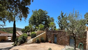 A courtyard with a stone staircase leading to a building with a blue door, surrounded by trees and plants. - Vacation apartment with large pool in the hills of the bay of St. Tropez (La Garde-Freinet)