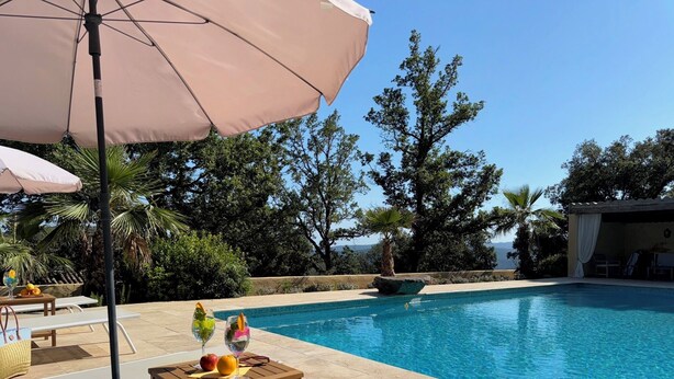 A poolside area with lounge chairs, a table with fruits and drinks, and a view of the ocean. - Vacation apartment with large pool in the hills of the bay of St. Tropez (La Garde-Freinet)