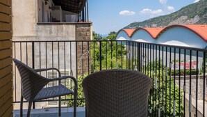 Un balcon avec des fauteuils en osier, une vue sur une montagne et un bâtiment avec un toit rouge.