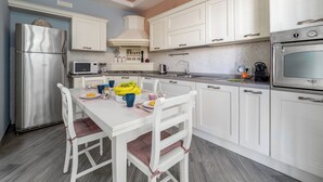 Une cuisine moderne avec des meubles blancs, des appareils en acier inoxydable et un coin repas comprenant des chaises blanches et une table dressée pour deux personnes.