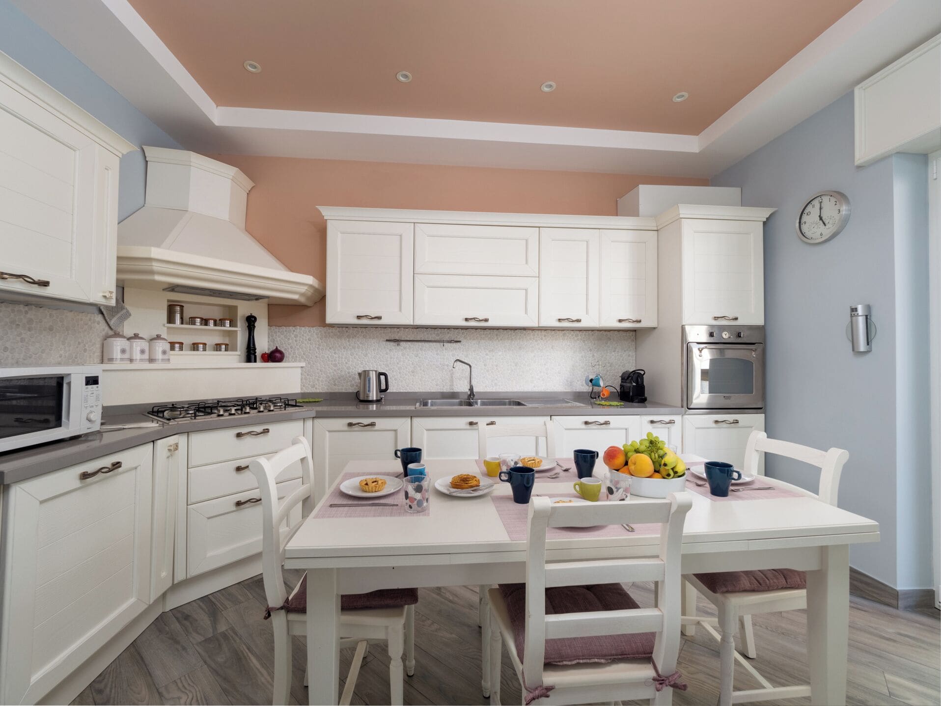Une cuisine moderne avec des meubles blancs, une cuisinière à gaz, un four à micro-ondes et une table à manger pour quatre personnes.
