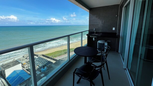 A balcony with a view of the ocean and beach, a small table and chairs, and a tiled backsplash. - RN STUDIO - APTO 1009 (Maceio)