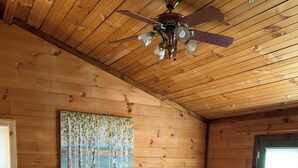 A wooden-paneled bedroom with a bed, two bedside tables, a ceiling fan, and a painting on the wall.