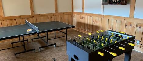 Una habitación con mesa de ping pong, mesa de fútbol de mesa y dardos.