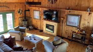 A cozy cabin interior with wooden walls, a stone fireplace, a television, and a ceiling fan.